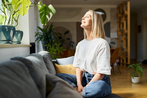 happy adult woman sitting on the sofa with eyes closed enjoying bright daylight showing  Deep Mind Healing Habits 