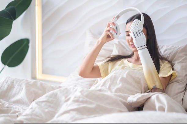happy girl with bionic arm relaxing listening music headphones in bed at home